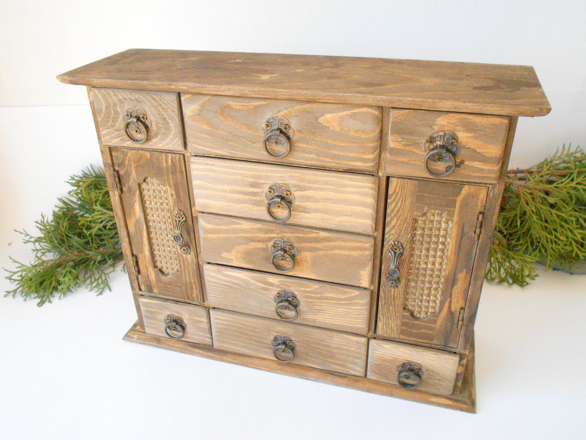 This wooden box with 9 drawers and 2 wardrobe doors is made of pinewood on the outside and bamboo wood for the inside of the drawers. It has metal pulls with a vintage bronze color. The surface of the box is smooth and refined with sanding paper. The color of the box is plain pinewood color.&amp;nbsp;