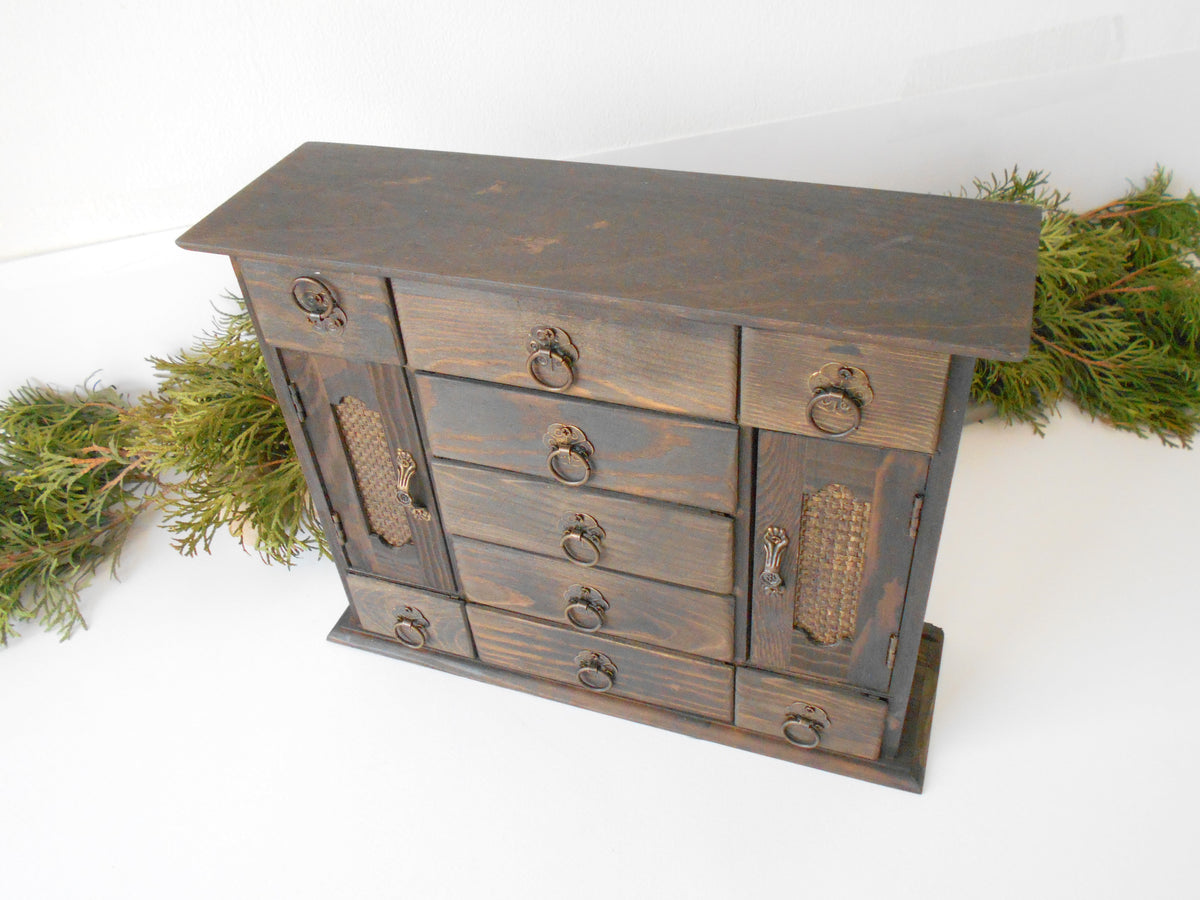 This wooden box with 9 drawers and 2 wardrobe doors is made of pinewood on the outside and bamboo wood for the inside of the drawers. It has metal pulls with a vintage bronze color. The surface of the box is smooth and refined with sanding paper.