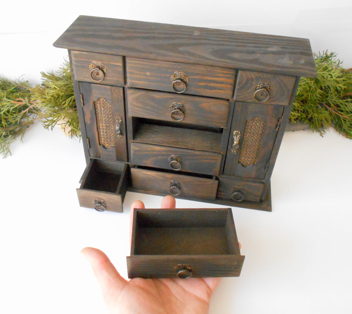 This wooden box with 9 drawers and 2 wardrobe doors is made of pinewood on the outside and bamboo wood for the inside of the drawers. It has metal pulls with a vintage bronze color. The surface of the box is smooth and refined with sanding paper.