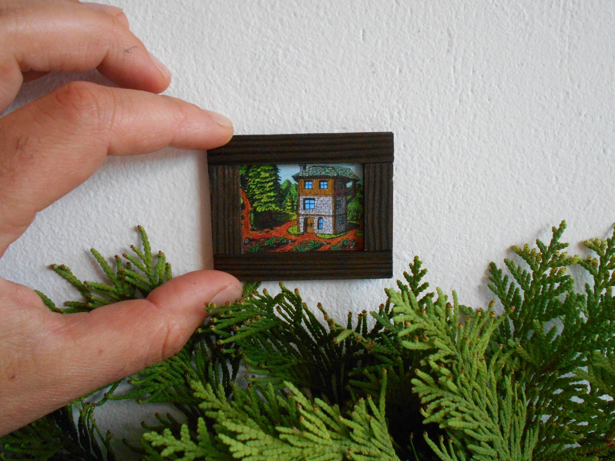 Handmade miniature wooden framed painting artwork for dollhouse collectors with an art of a mountain landscape and a logghouse hut cottage and a garden by ExiArts eco-friendly company from Bulgaria.