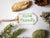 Handmade hang tag with hand-written eco-friendly word on it and surrounded by a pine branch, pine cone, stones and lichen 