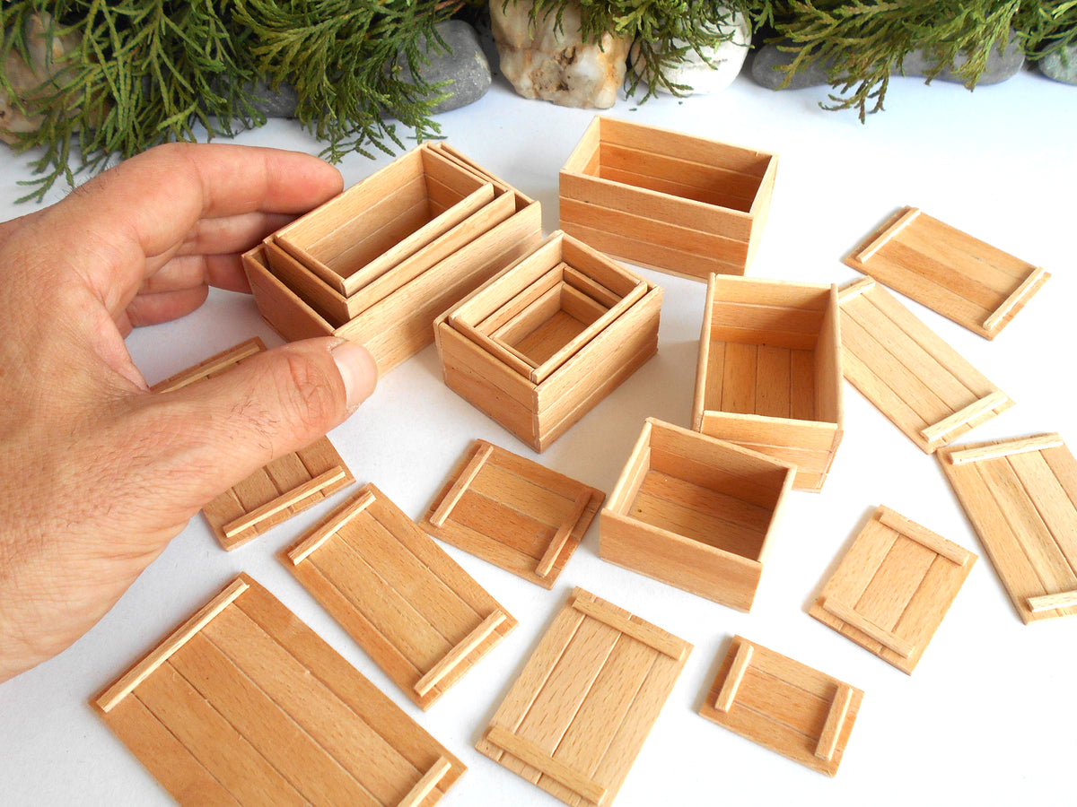 A hand holding a set of small wooden miniature boxes , with several matching wooden boxes scattered on a white surface in the background.