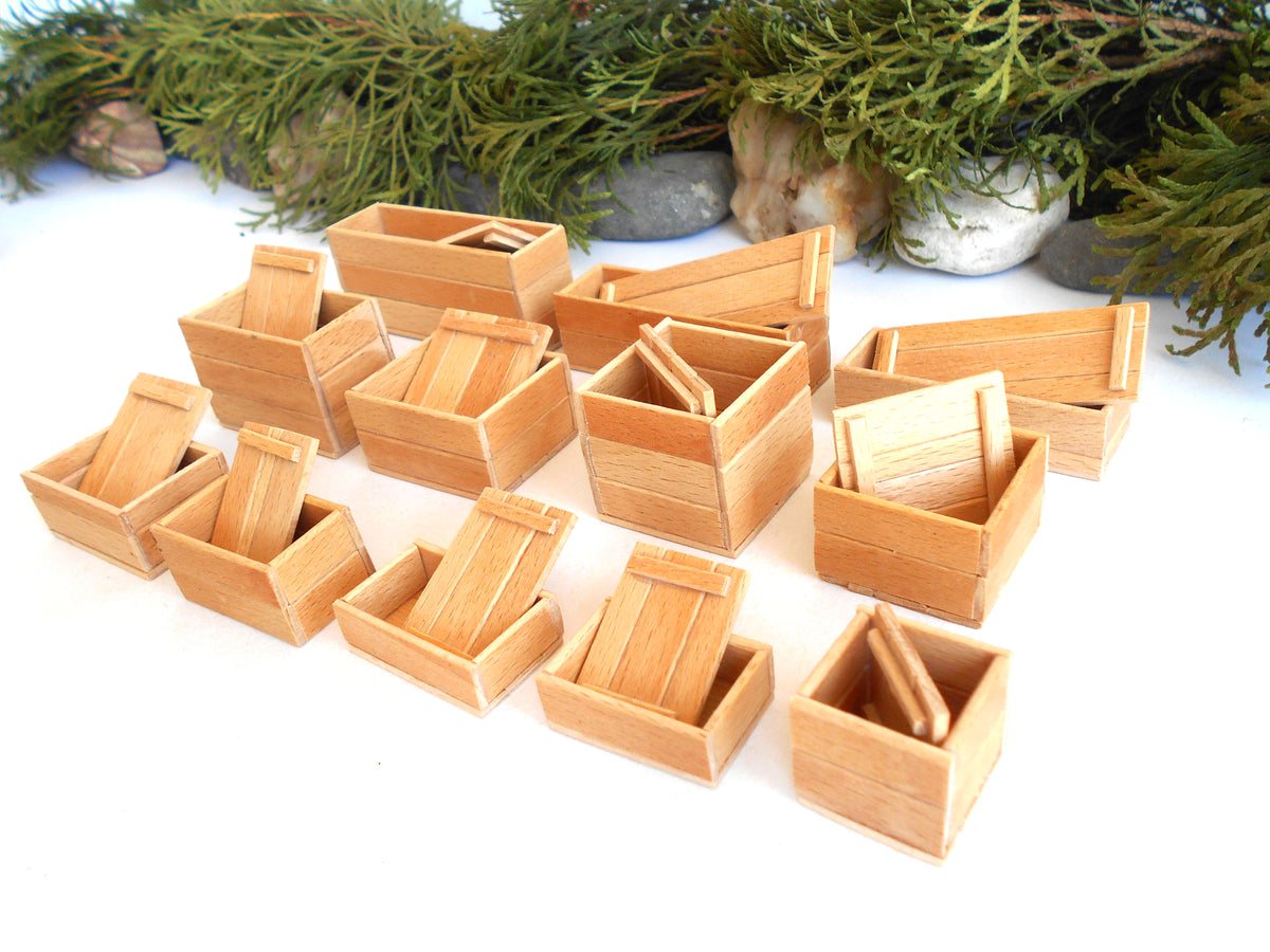 A set of miniature light wood boxes, including some open-top crates and one small wooden ladder, arranged on a white surface with a decorative green pine garland in the background.