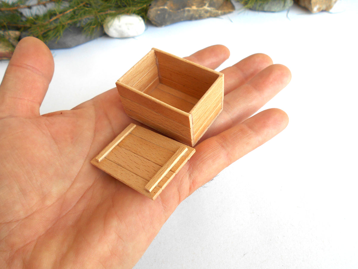 A miniature light brown wooden box with its lid placed beside it, held in a person's hand to show its small scale.