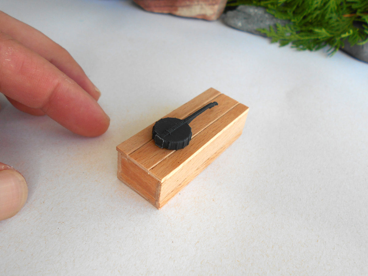 A miniature wooden model tank with a black turret, shown on a white surface next to a person's fingers for scale.