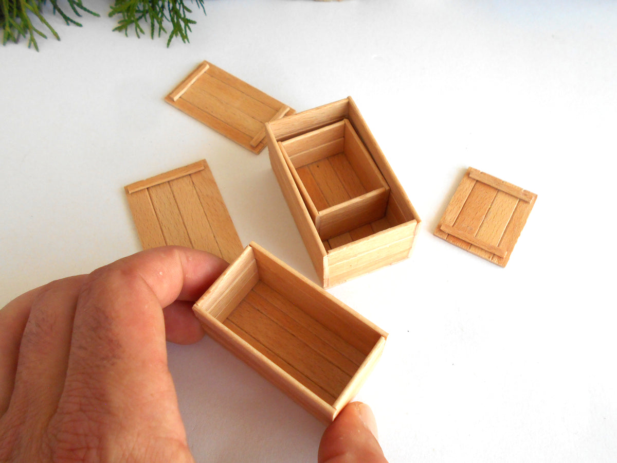A close-up of a hand holding a miniature light wood box, with several matching small wooden boxes and lids arranged on a white surface.