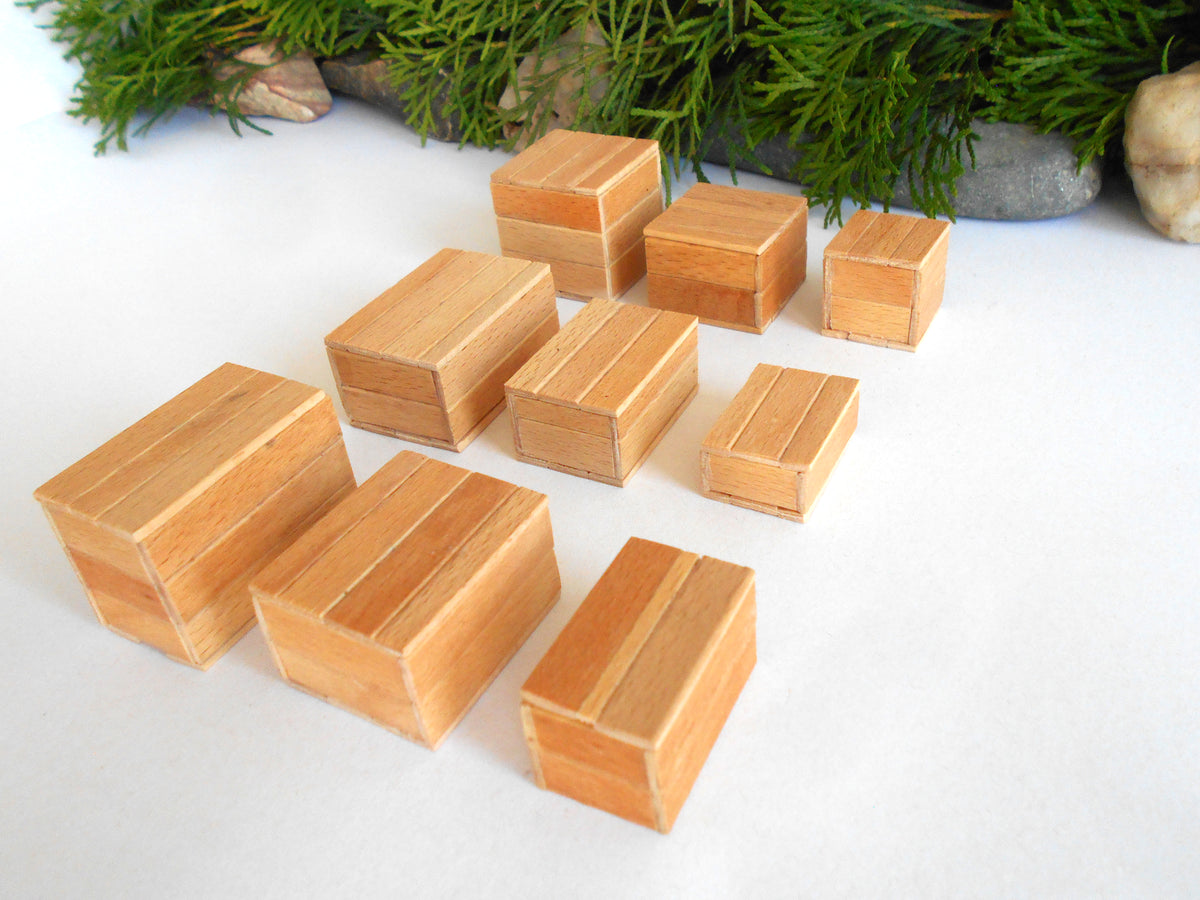 A set of small wooden boxes with a striped grain pattern, arranged on a white surface with green foliage and stones in the background.