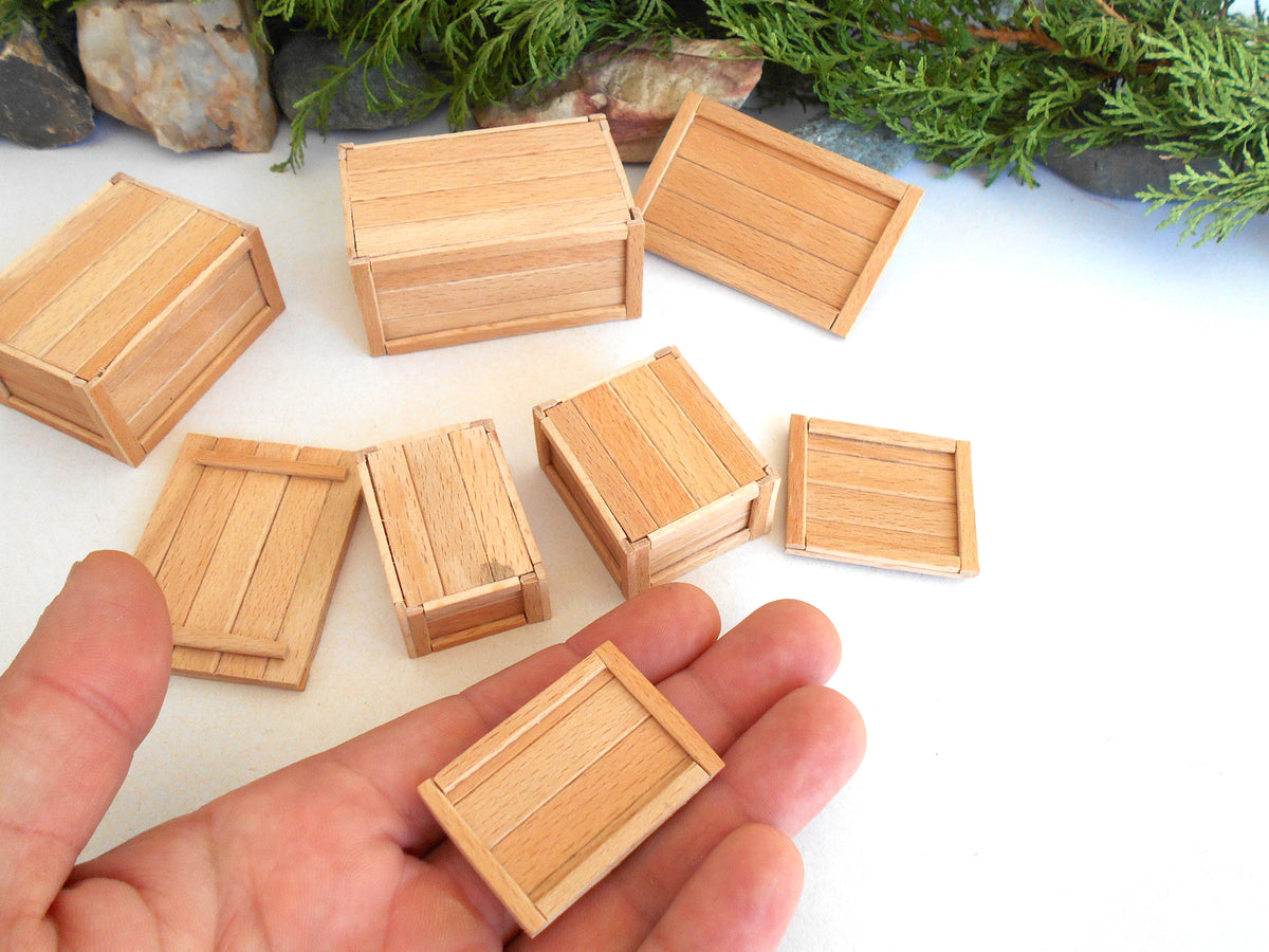 A hand holding a miniature light wood box, with several other matching small wooden boxes scattered on a white surface in the background.