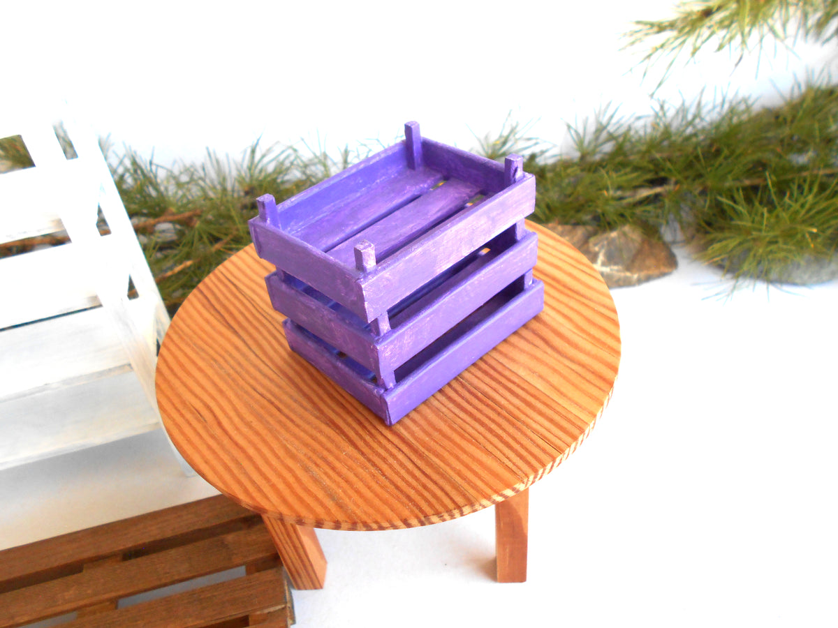 Three stacked purple wooden crates displayed on a round wooden table against a white background with decorative greenery.