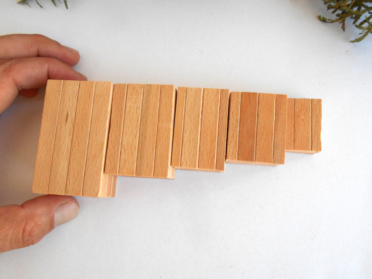 A hand holding a set of light natural wood rectangular miniature boxes with vertical grooves, arranged in a descending size sequence on a white background.