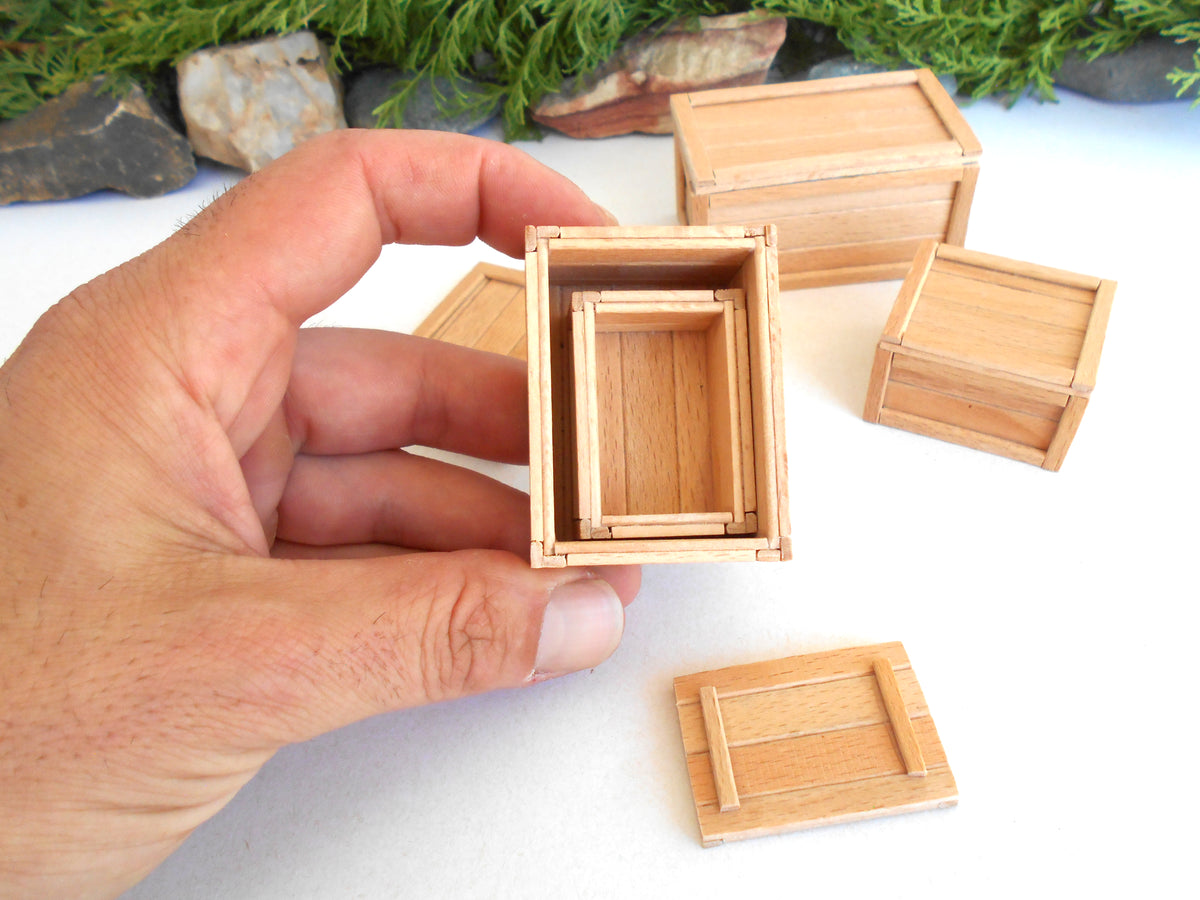 A hand holding a miniature wooden box frame, with several matching small wooden boxes arranged on a white surface in the background.
