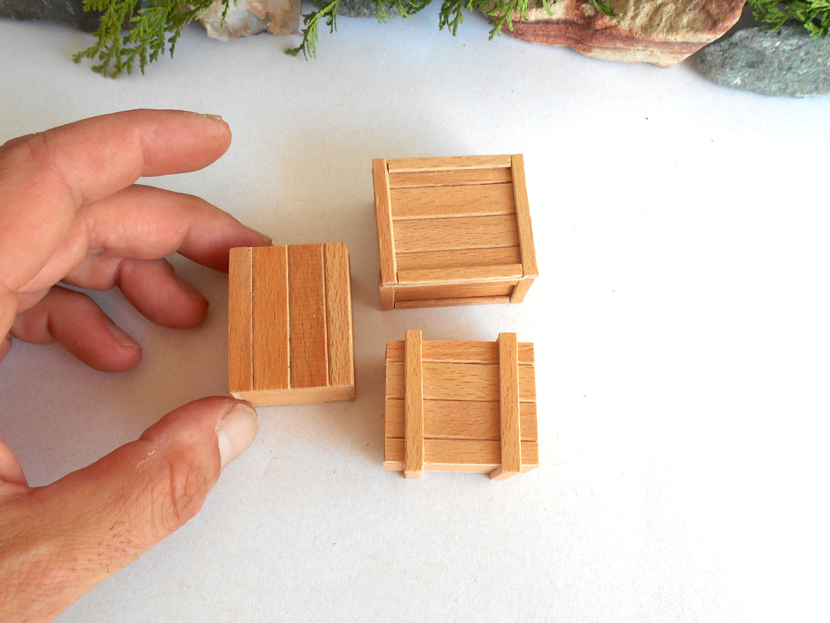 Three miniature wooden crates in different sizes, with a hand holding one of the smaller crates to show scale, on a white surface.