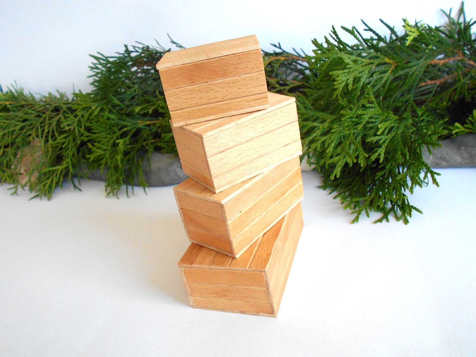 A stack of four nested rectangular wooden boxes in varying sizes, styled with green pine branches on a white surface against a white background.