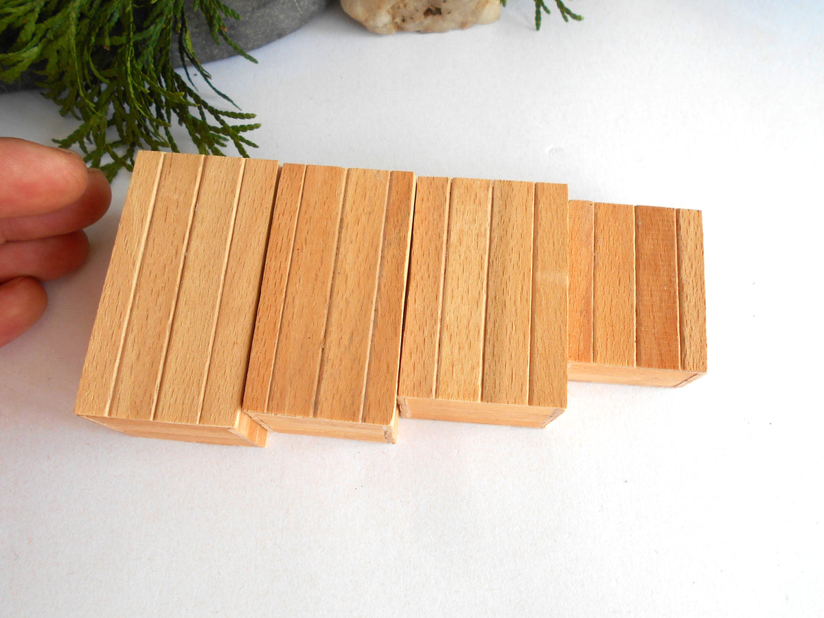 Four rectangular mini wooden boxes with vertical grooves, arranged in a staggered row on a white surface, with a hand holding one block on the left.
