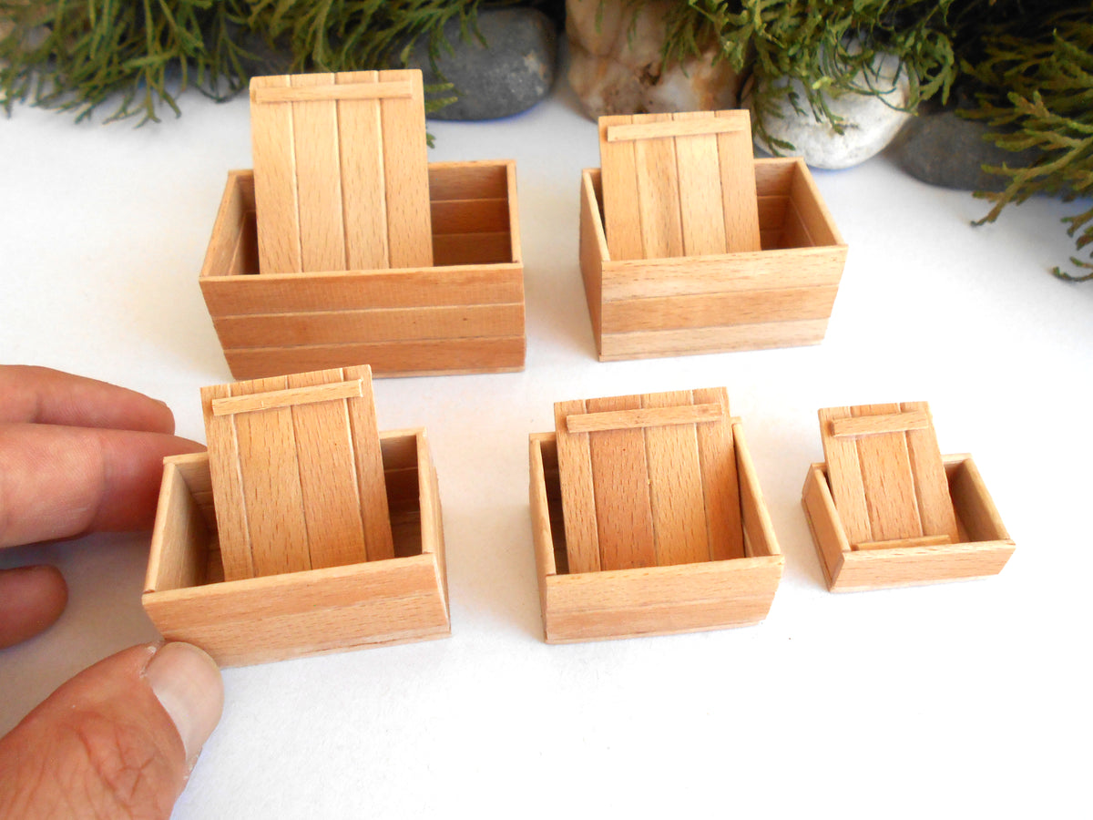 Six miniature wooden box lids with slatted fronts, shown in various sizes on a white surface with a hand holding one of the smaller boxes for scale.