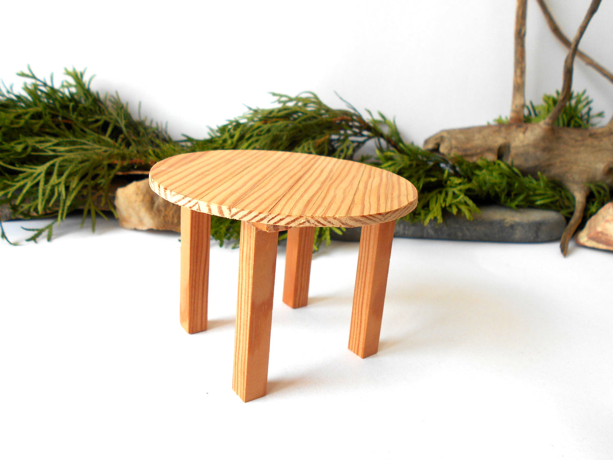 A small round wooden stool with a light natural wood grain finish, featuring a circular seat and four tapered legs, set against a white background with decorative greenery.