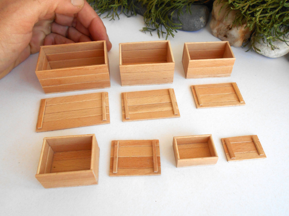 A set of miniature light wood boxes and trays in various sizes, displayed on a white surface with a hand holding one of the larger boxes for scale.
