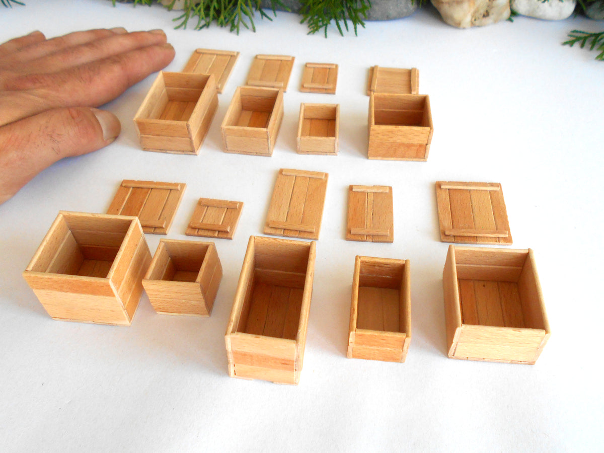 A set of miniature light wood boxes and crates in various sizes, displayed on a white surface with a person's hand visible on the left for scale.