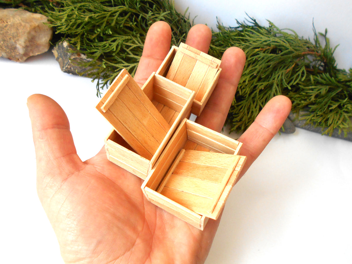 A hand holding several miniature light wood boxes, with green foliage and rocks in the background.