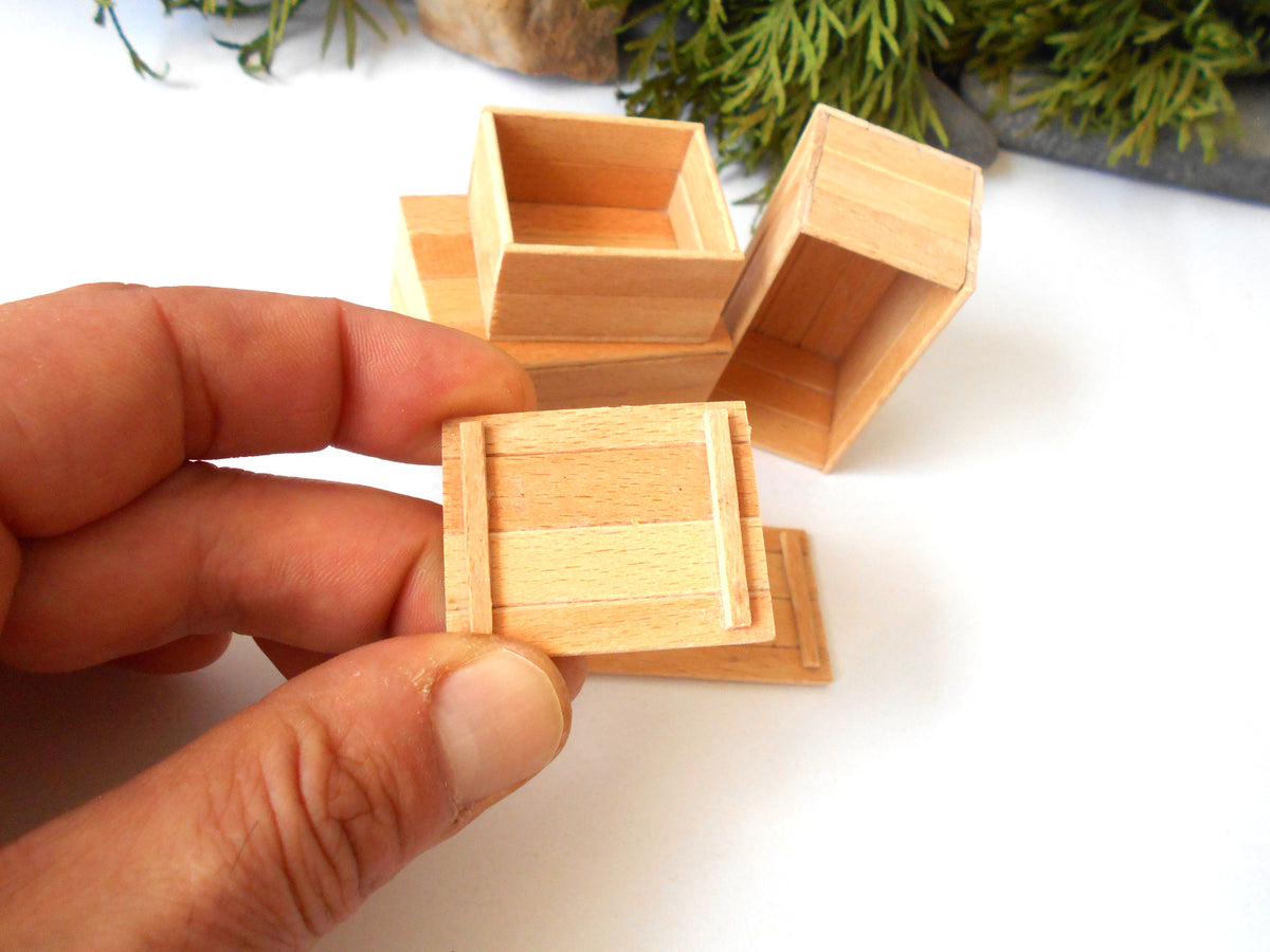 A hand holding a small unfinished wooden box, with two more matching wooden boxes in the background on a white surface.