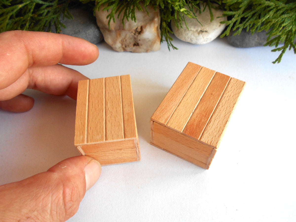 Two miniature wooden matchboxes with a vertical plank design, shown on a white surface with a hand holding one of them for scale.