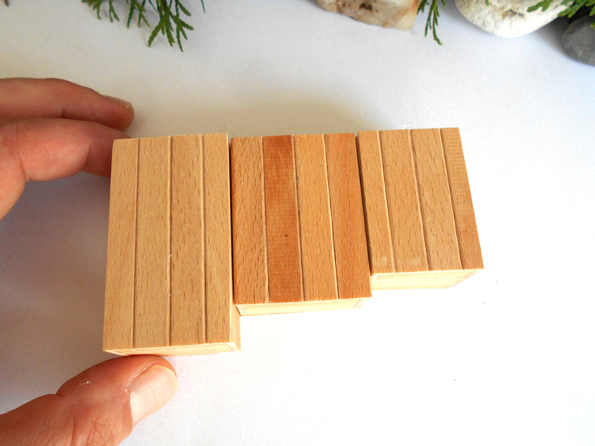 Three rectangular wooden boxes with vertical grooves, showing natural wood grain in light tan and medium brown tones, held by a person's hand on a white surface.