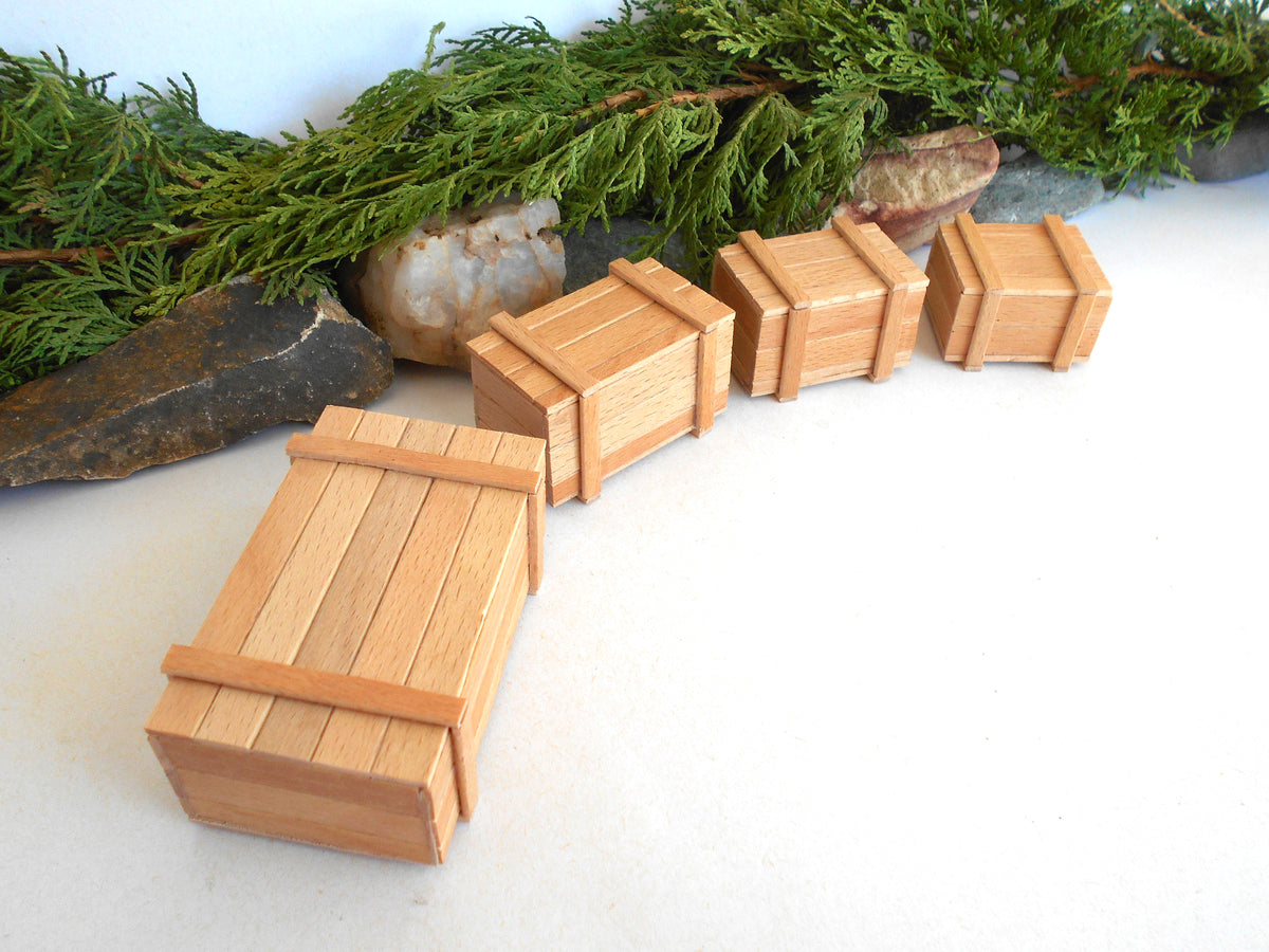 Five miniature wooden crates of varying sizes arranged on a white surface with green foliage and rocks in the background.