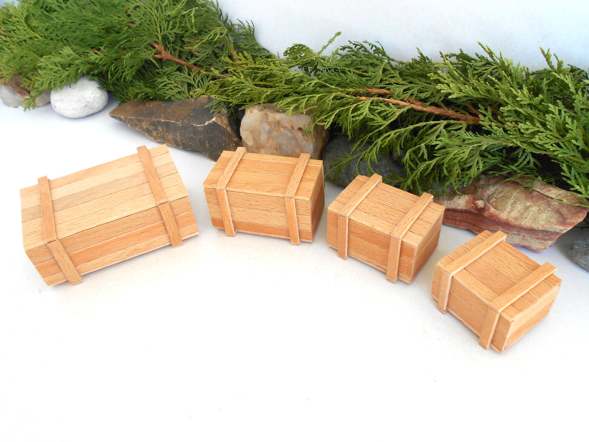 Four miniature light wood boxes of varying sizes arranged on a white surface with green pine branches and small stones in the background.