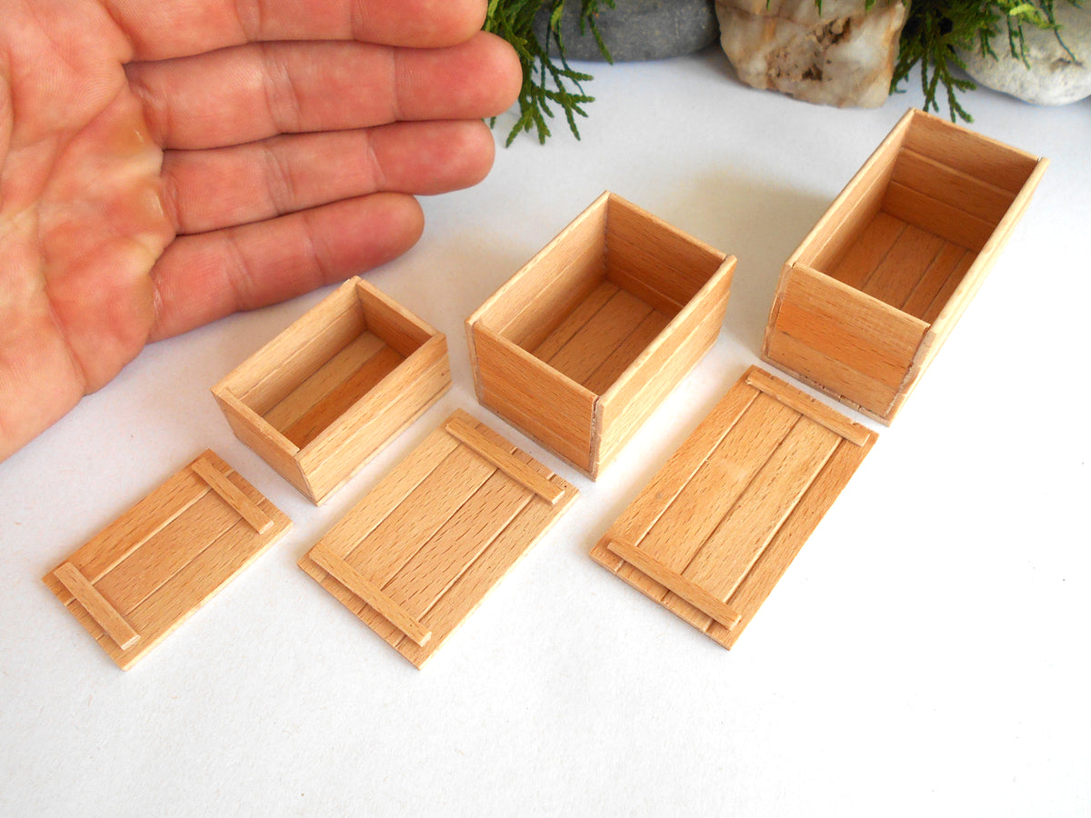 Six miniature light wood boxes and matching lids in various rectangular sizes, displayed on a white surface with a human hand visible for scale on the left.