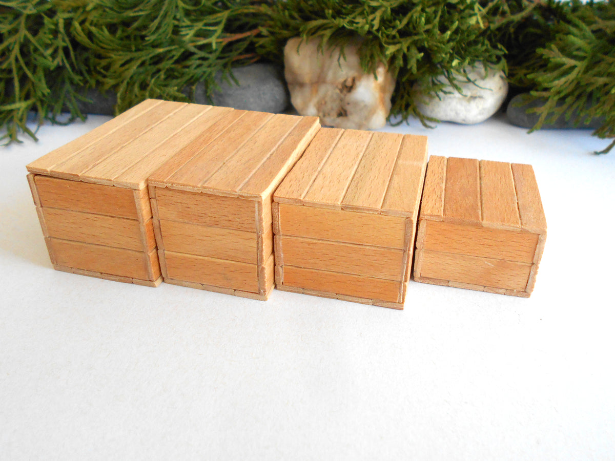 Four miniature wooden boxes of varying sizes arranged in a row on a white surface, with green foliage and small stones in the background.