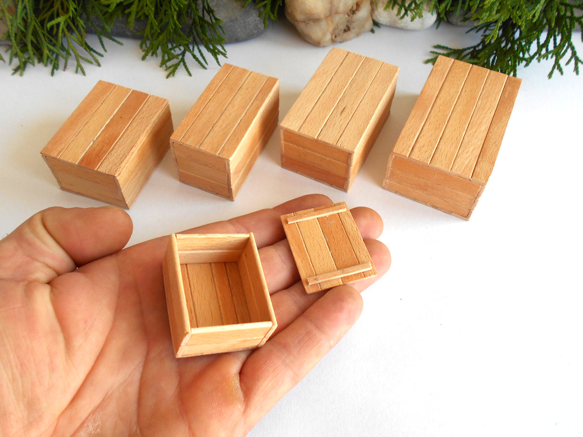 Five miniature light wood boxes of different sizes, including one open box and one closed box, displayed on a white surface with a hand holding two of the smaller boxes for scale.