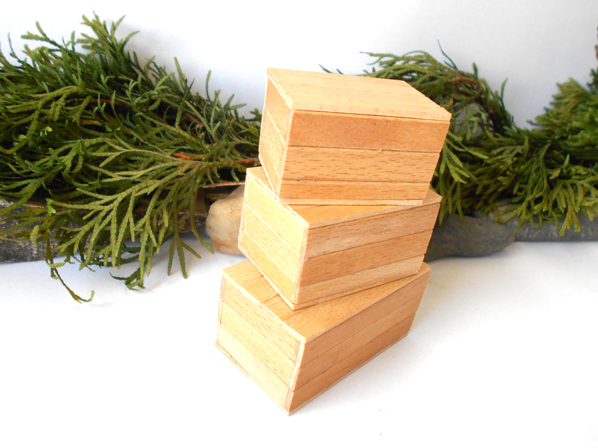 Four small rectangular wooden boxes stacked in a staggered arrangement, with a green garland and small stones in the background on a white surface.