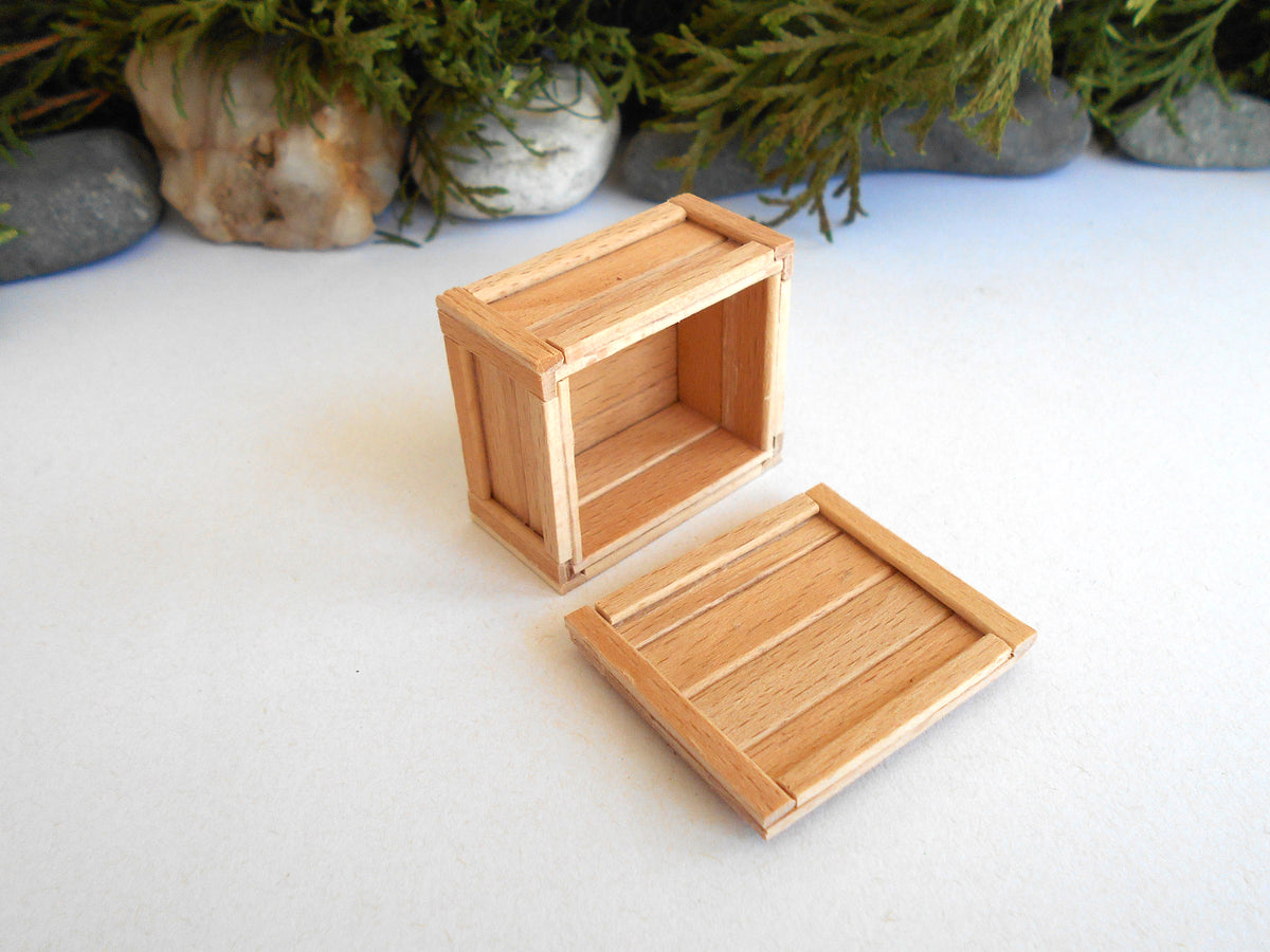 A miniature light wood crate box with its lid off, displayed on a white surface with decorative moss and stones in the background.