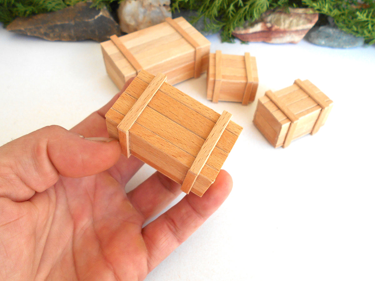 A hand holding a miniature wooden crate model, with several smaller matching crate models placed on a white surface in the background.