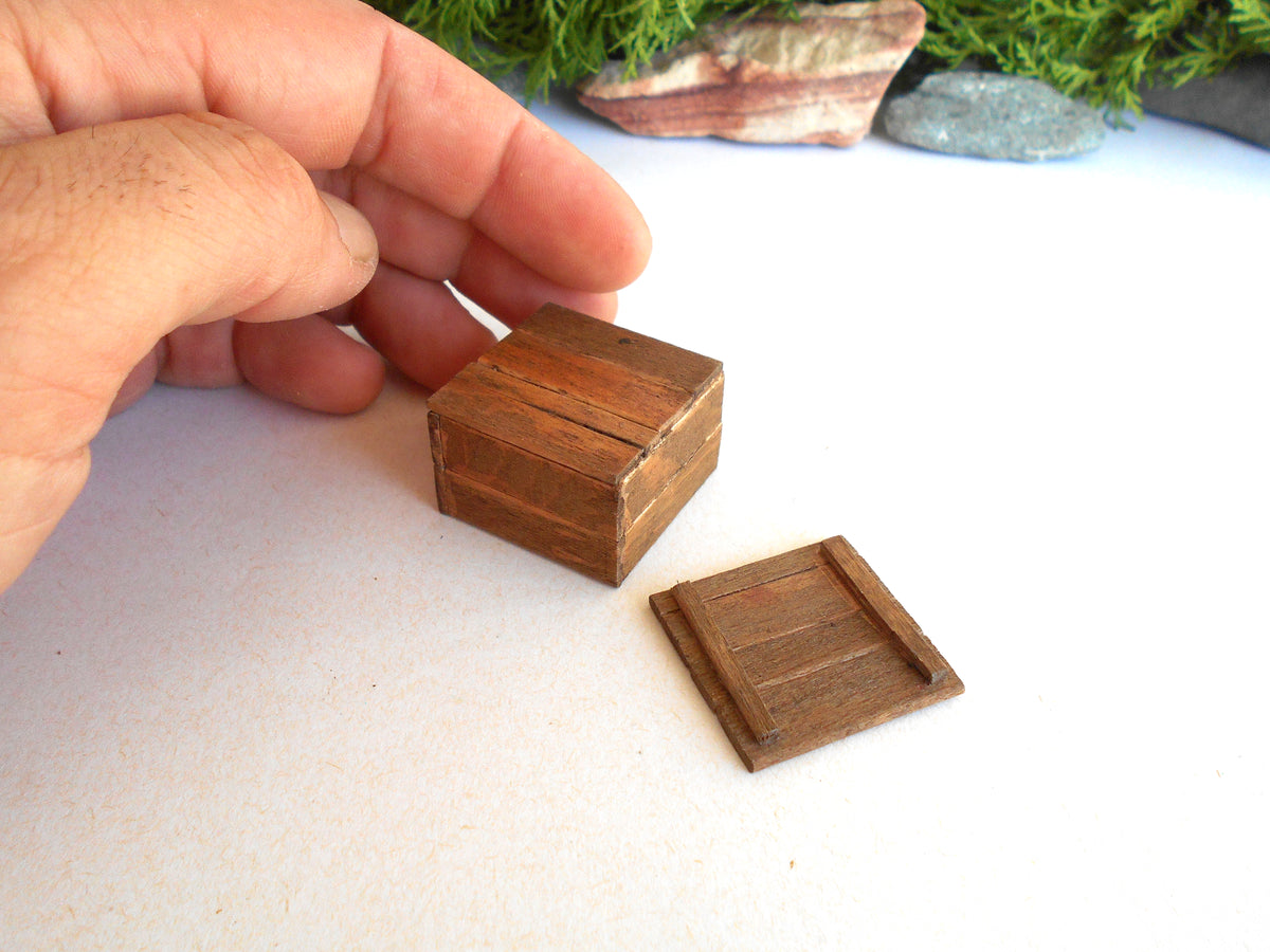 A miniature wooden box with a matching lid, shown with a human hand holding it for scale on a white surface.