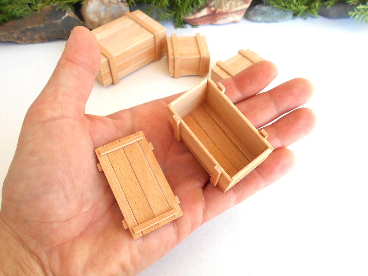 A hand holding several miniature light wood crates and boxes, with more of the same boxes in the background on a white surface.