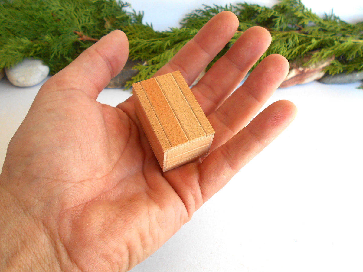 A small rectangular wooden block with three parallel grooves, held in the palm of a hand against a white background with green foliage in the distance.