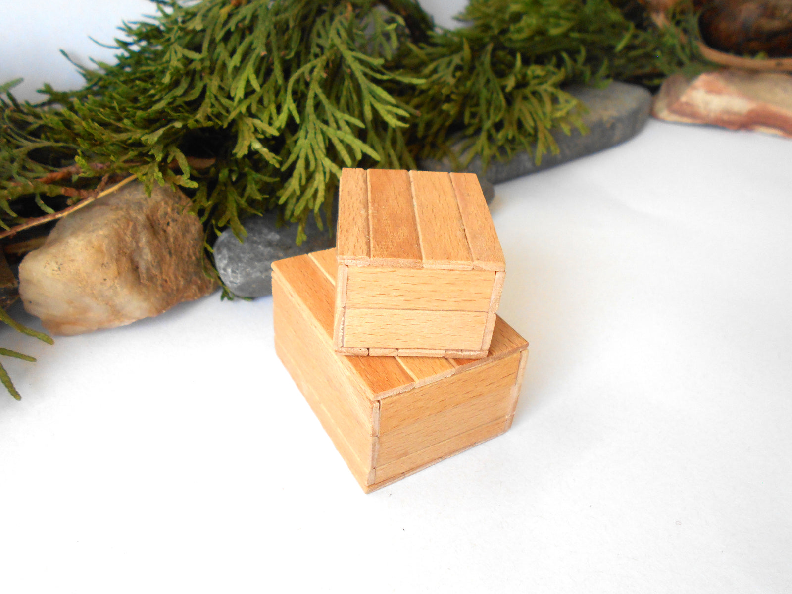 Two small stacked wooden boxes with a natural light oak finish, set against a white background with decorative green foliage and stones.