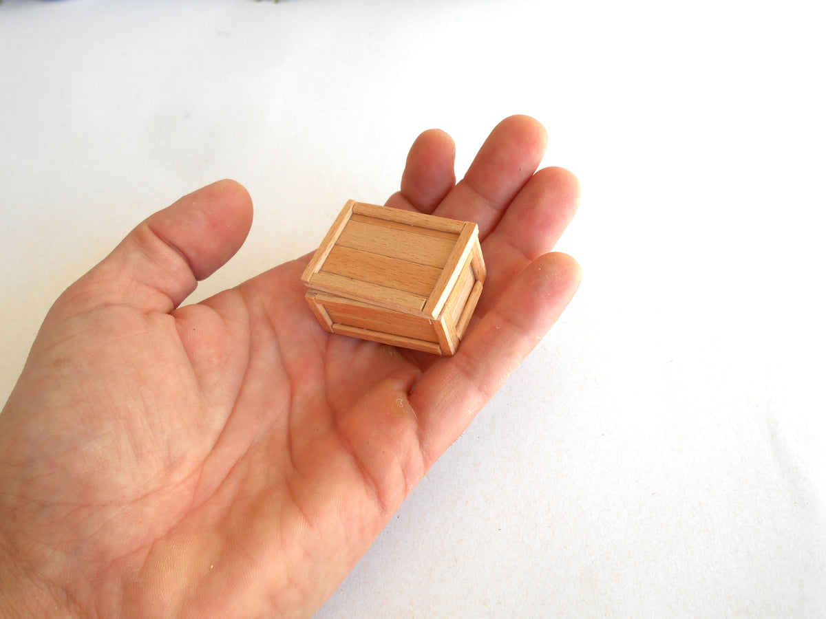A miniature light wood crate toy or model held in a person's hand against a plain white background.