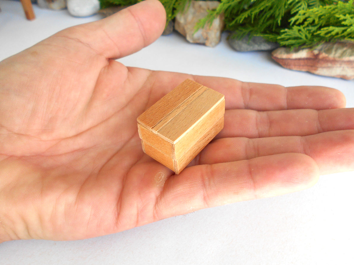 A miniature light brown wooden box with a slatted top, held in the palm of a hand to show its small scale.