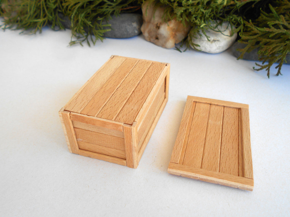 A miniature wooden storage box with a matching lid, shown on a white surface with decorative greenery in the background.