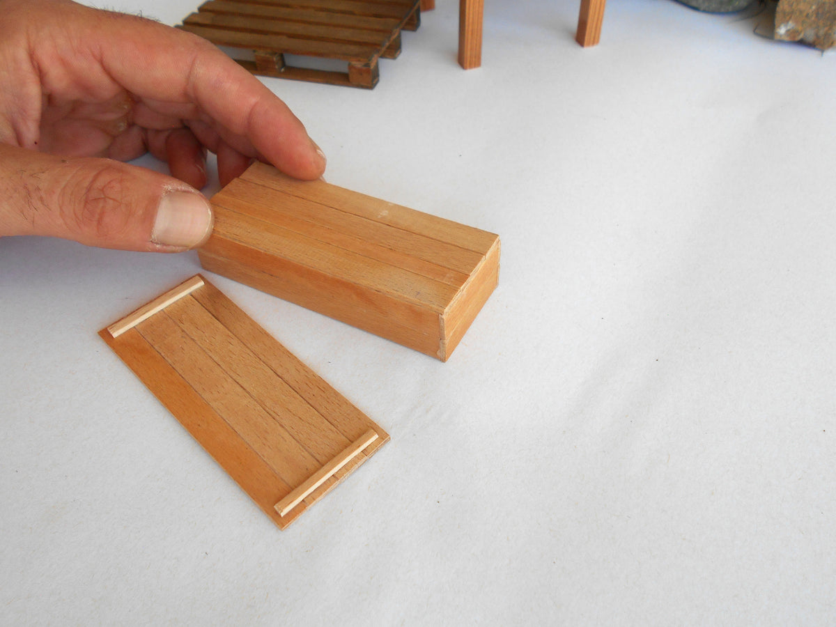 A close-up of a hand holding a small rectangular wooden block above another matching wooden piece on a white surface.