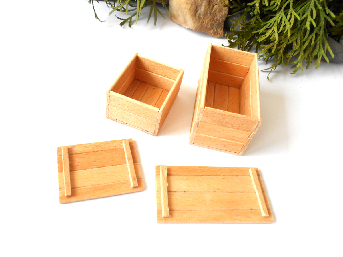 Four small light wood boxes and two matching lids arranged on a white surface, with greenery and a rock prop in the background.