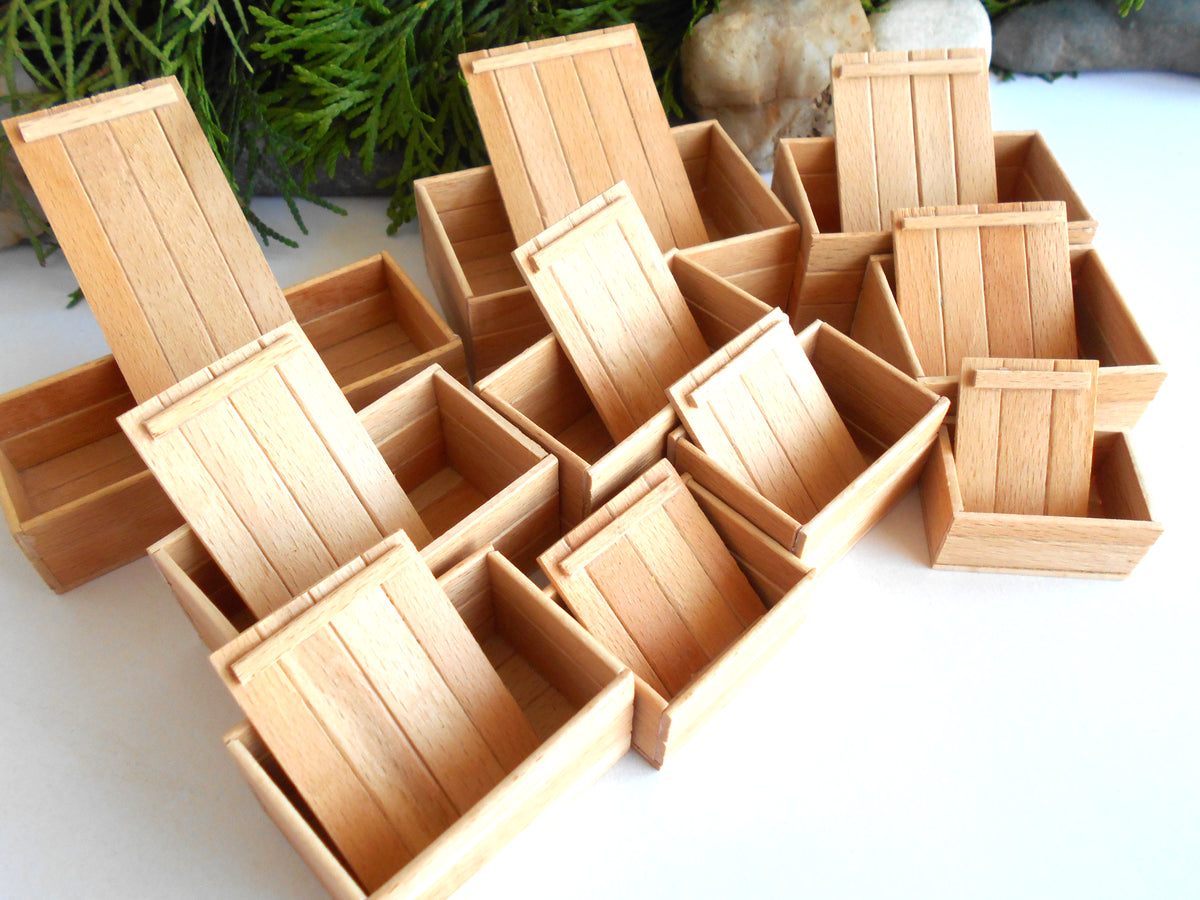 A group of miniature light wood crate dollhouse accessories arranged on a white surface with some green foliage and stones in the background.