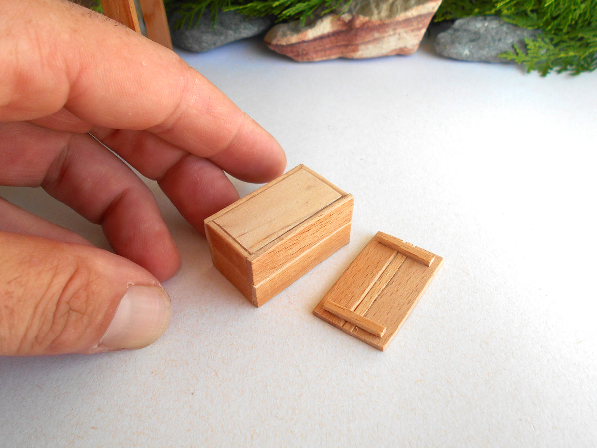 A close-up of a hand holding a miniature wooden box next to its matching lid, which is shown to be quite small in scale.