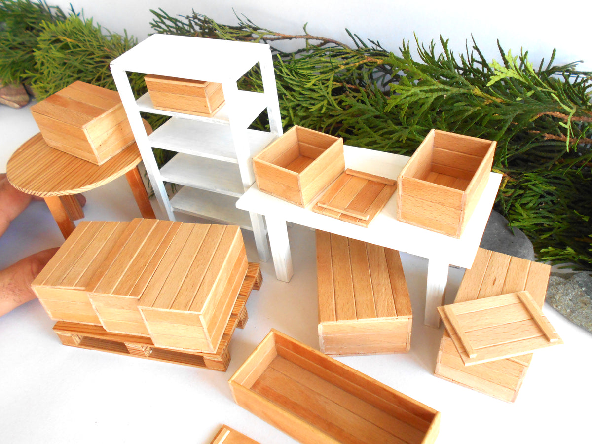 A set of miniature wooden storage boxes, crates, and shelving units displayed on a white surface with green foliage in the background.