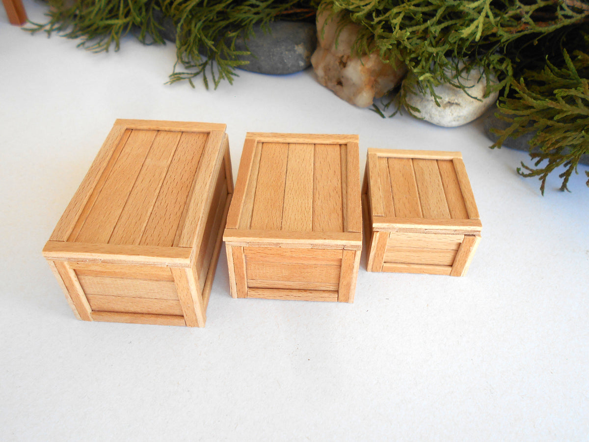 Three small natural wood crates of different sizes arranged on a white surface with green foliage and stones in the background.