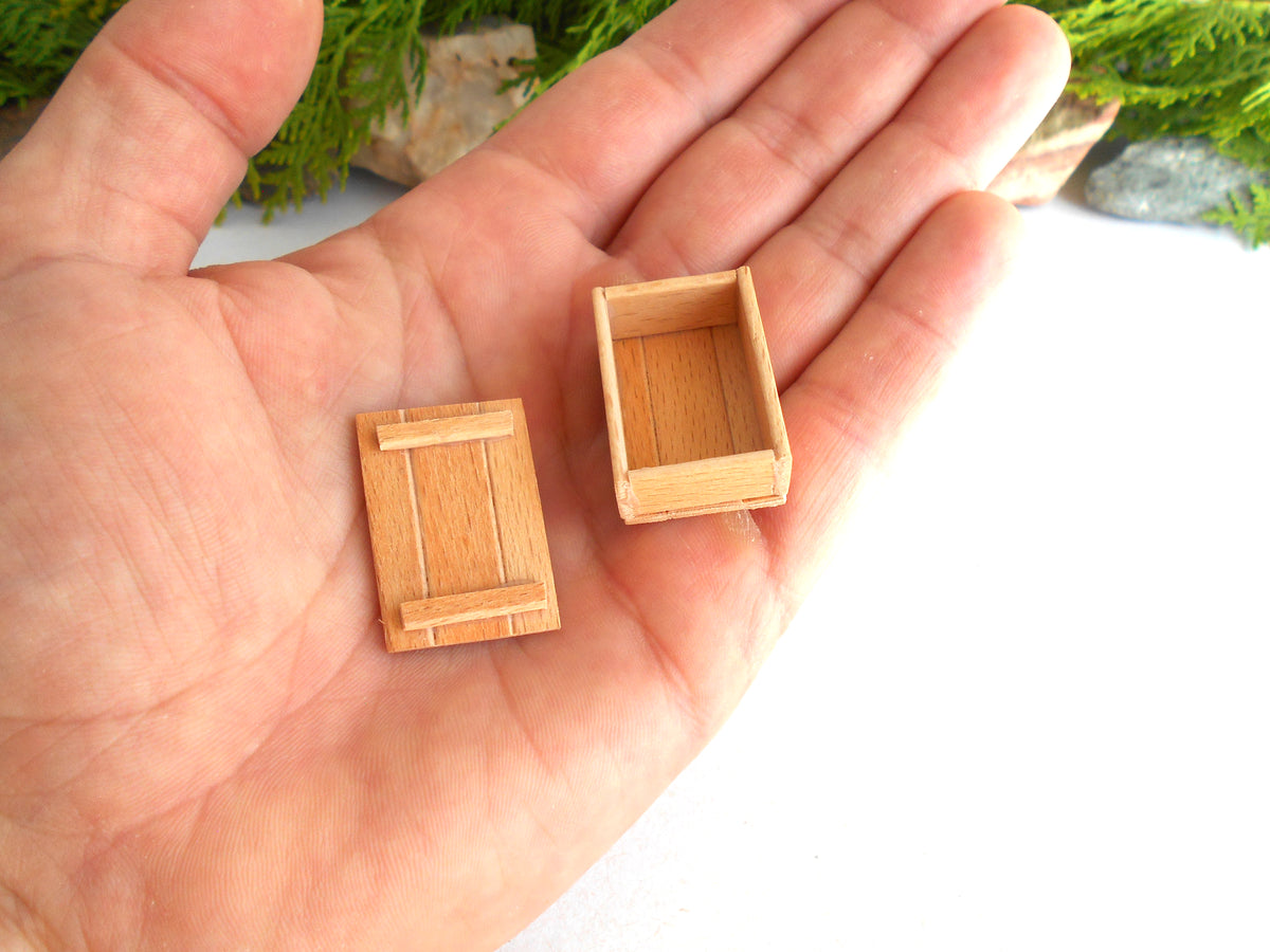 Two miniature light brown wooden boxes, one closed and one open, displayed on a person's palm to show their small scale.