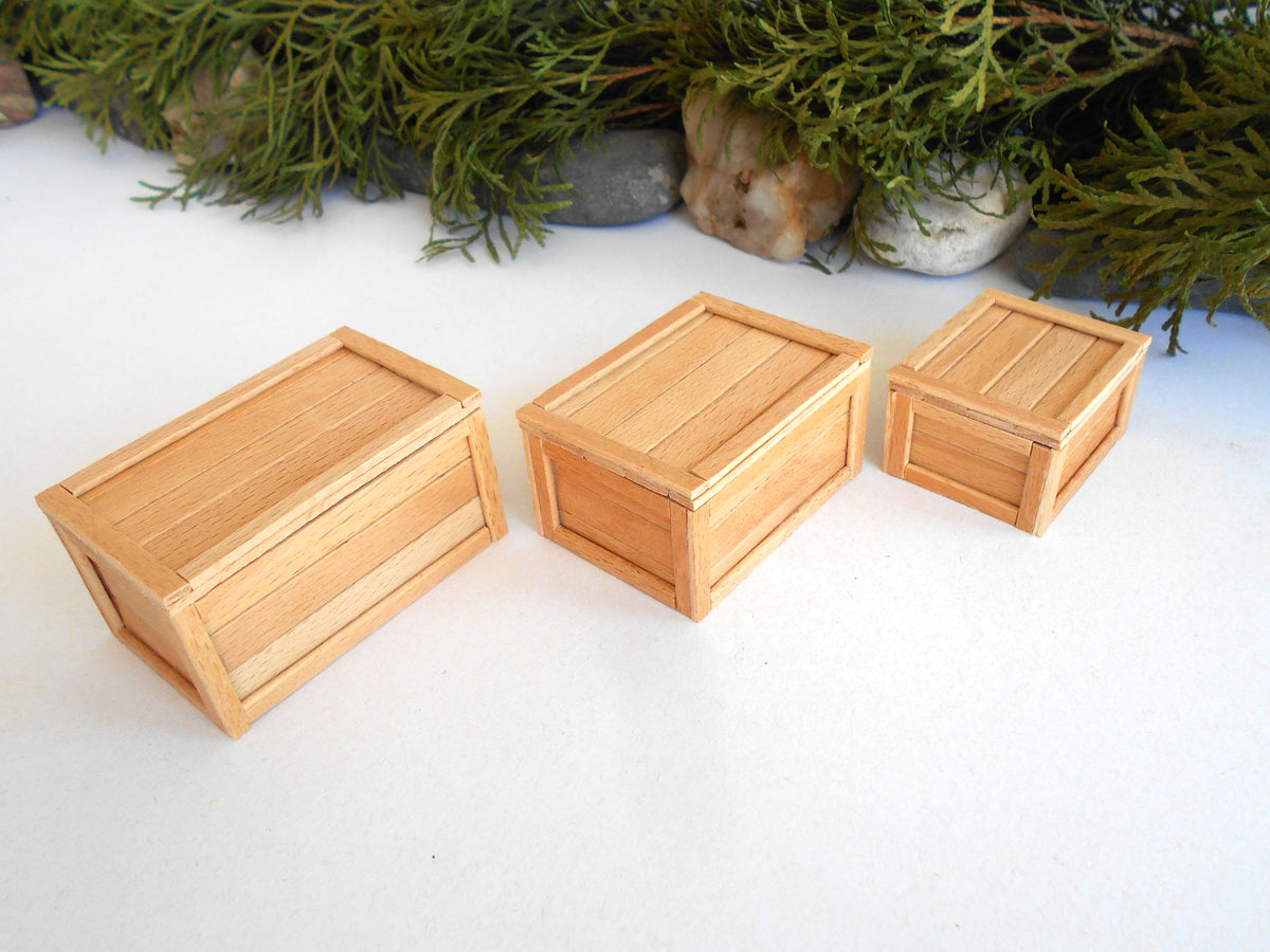 Three miniature wooden crates in different sizes arranged on a white surface with green foliage and small stones in the background.
