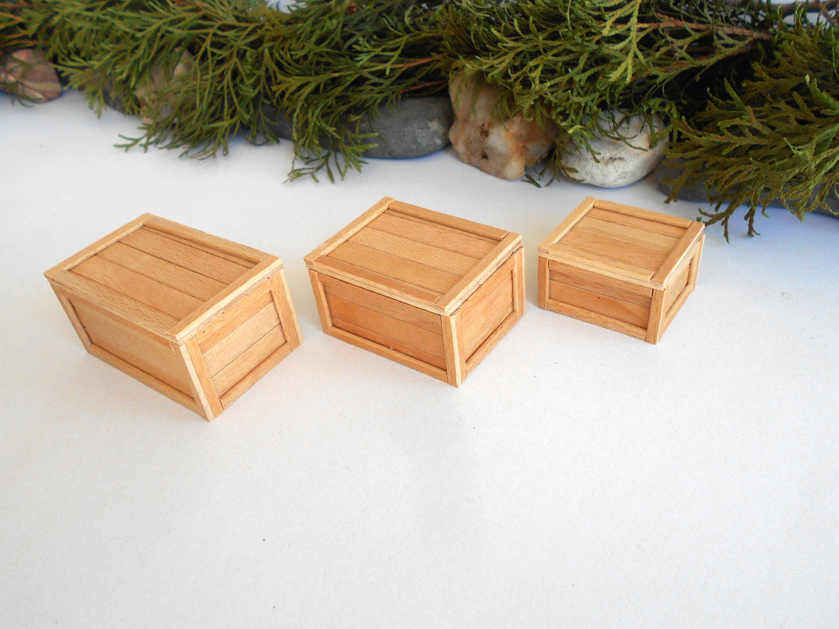 Three small natural wood crates of different sizes arranged on a white surface with green foliage and stones in the background.